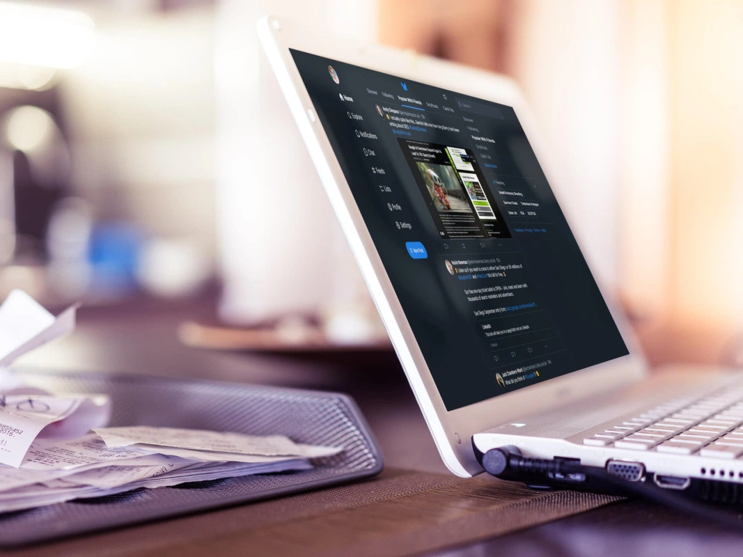 A laptop displaying a Bluesky feed sits on a desk next to a tray full of receipts. (Captioned by AI)
