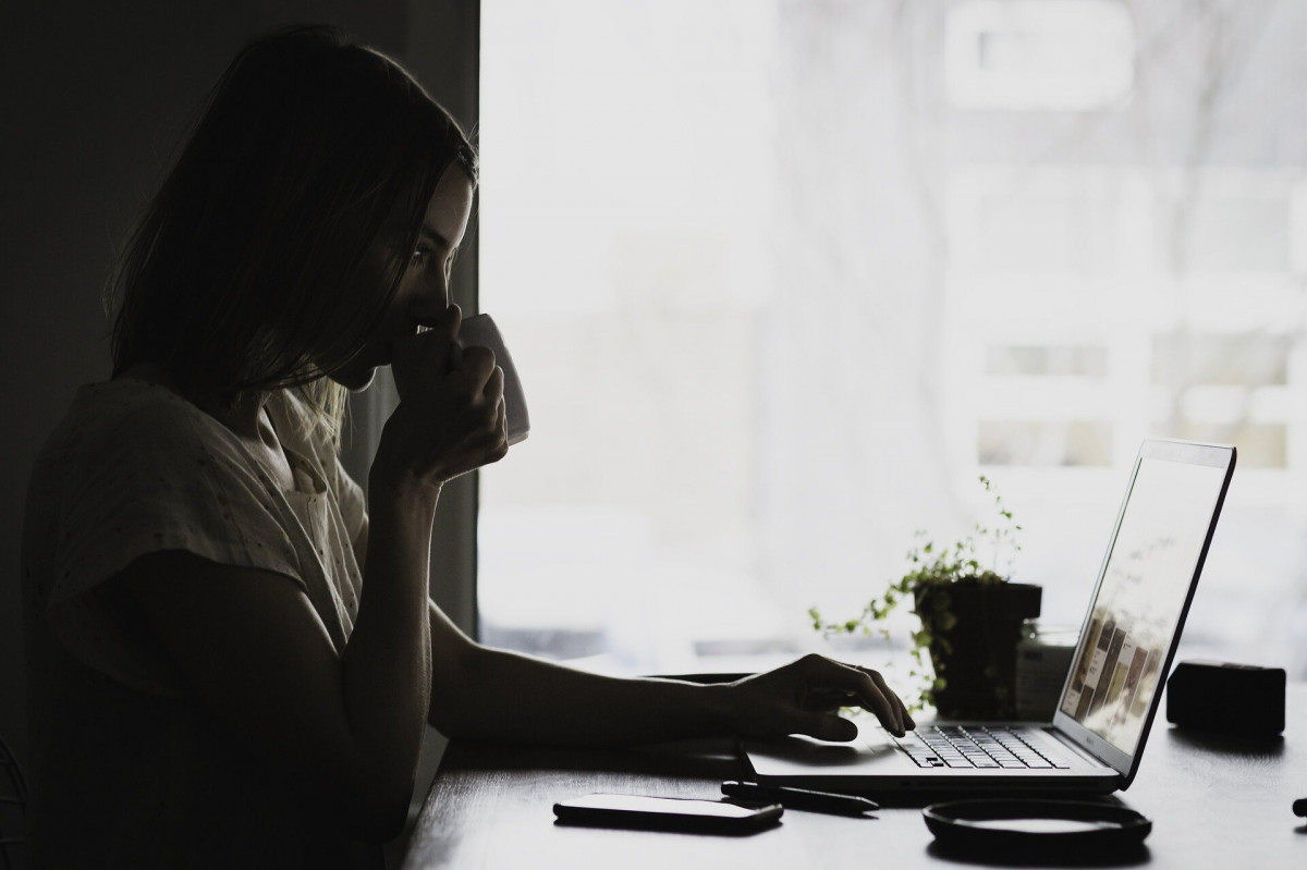 A woman drinking from a mug while using a laptop